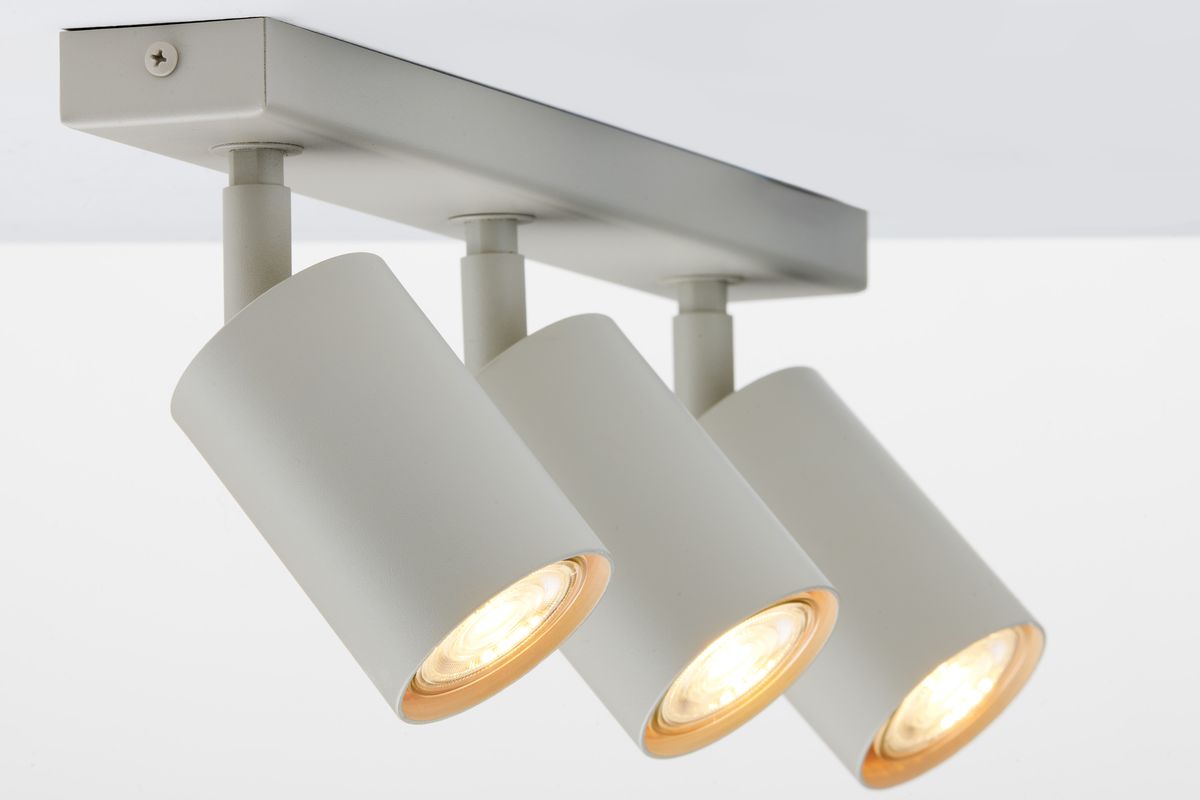 Lampa sufitowa typu spot w kolorze szarym beżowym, z trzema reflektorami GU10. Ujęcie z boku, ukazujące cylindryczne klosze z widocznym światłem. Montaż na prostokątnej podstawie, idealna do oświetlenia wnętrza.