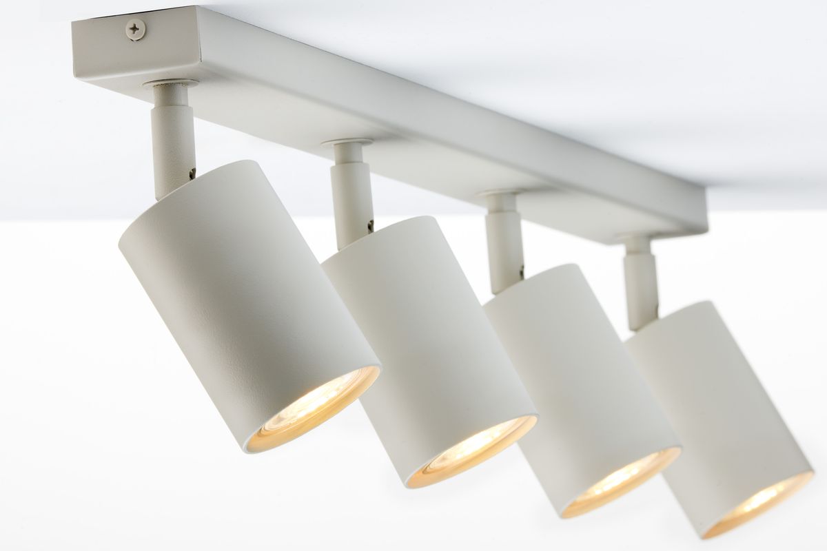 Lampa sufitowa Zoom z czterema reflektorami GU10 w kolorze szarym beżowym. Reflektory mają cylindryczny kształt, są zamontowane na prostokątnej podstawie. Widoczne ciepłe światło w każdej lampie. Ujęcie z dołu, ukazujące szczegóły konstrukcji.