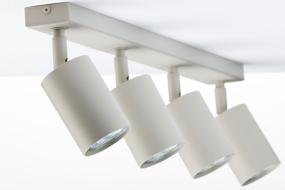 Lampa sufitowa Zoom w kolorze szarym beżowym z czterema reflektorami GU10. Reflektory są cylindryczne, zamocowane na prostokątnej listwie. Ujęcie z dołu, pokazujące detal konstrukcji i kąt nachylenia lamp.