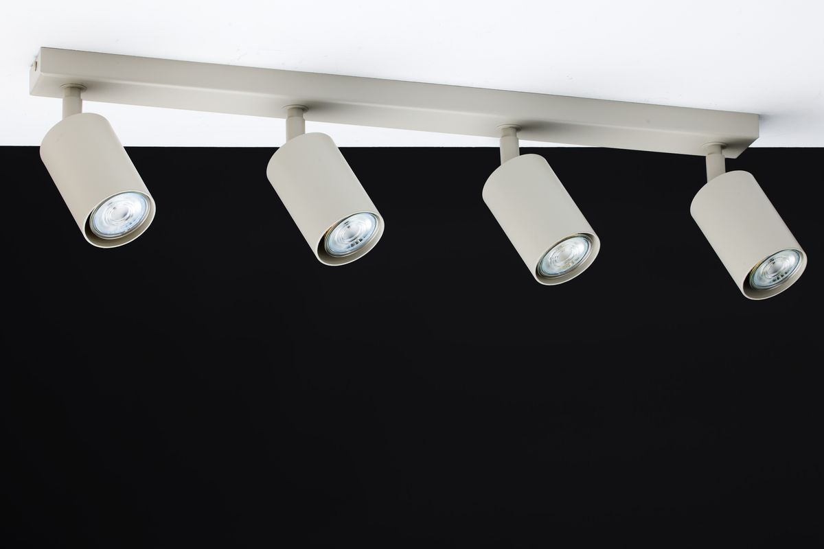 Lampa sufitowa Zoom w kolorze szarym beżowym z czterema regulowanymi reflektorami GU10. Ujęcie z góry, zamontowana na prostokątnej listwie. Reflektory mają cylindryczny kształt, co umożliwia kierunkowe oświetlenie. Tło czarne.