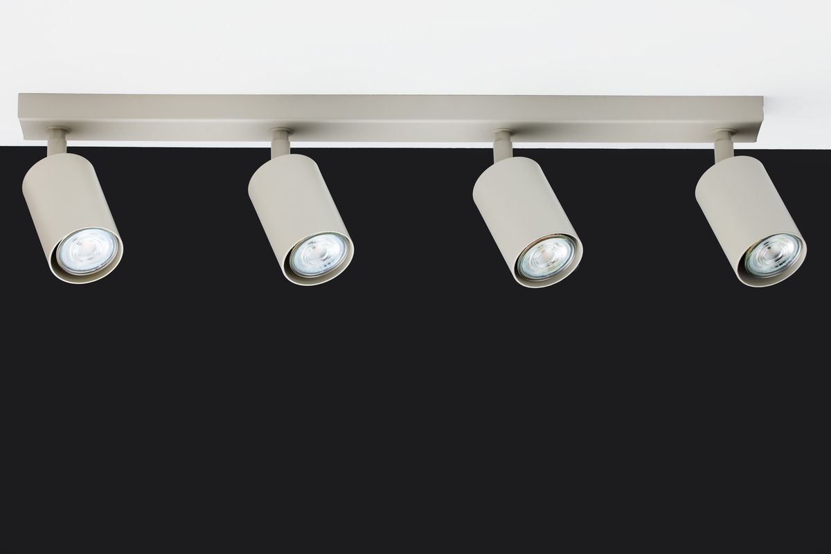 Lampy sufitowe Zoom w kolorze szarym beżowym, z czterema reflektorami GU10, zamontowane na prostokątnej, metalowej podstawie. Ujęcie frontalne, ukazujące lampy skierowane w dół, na jednolitym czarnym tle.