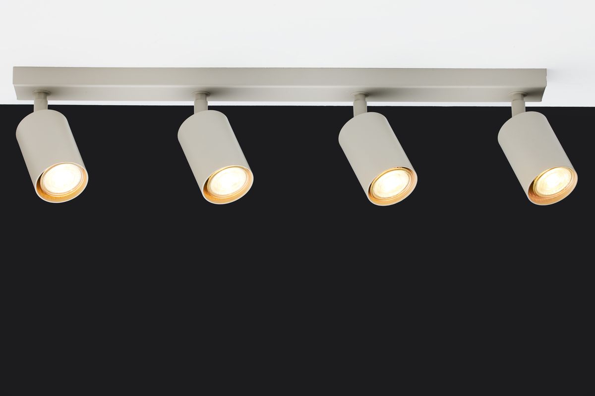 Lampa sufitowa Zoom w kolorze szarym beżowym, z czterema punktami świetlnymi GU10. Ułożona poziomo, z cylindrycznymi kloszami skierowanymi w dół, montowana na prostokątnej podstawie. Tło ciemne, co podkreśla jasne światło lampy.