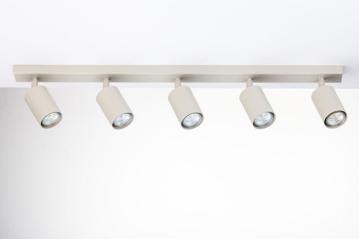 Lampa sufitowa typu spot w kolorze szarym beżowym z pięcioma źródłami światła GU10, zamontowana na prostokątnej, płaskiej podstawie. Klosze mają cylindryczny kształt, skierowane w różnych kierunkach. Tło zdjęcia jest jasne i jednolite.