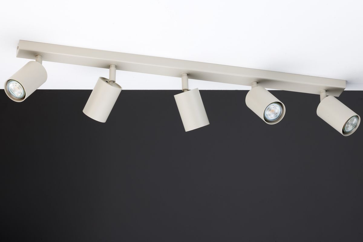 Lampa sufitowa Zoom w kolorze szarym beżowym z pięcioma reflektorami GU10. Ujęcie z boku, mocowana do sufitu. Reflektory są cylindryczne, skierowane w różnych kierunkach, na tle ciemnej ściany.