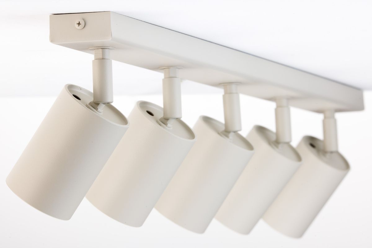 Lampa sufitowa w kolorze szarym beżowym z pięcioma ruchomymi spotami na szynach. Każdy spot ma cylindryczny kształt i gładką, matową powierzchnię. Ujęcie z góry, ukazujące montaż lampy do sufitu.