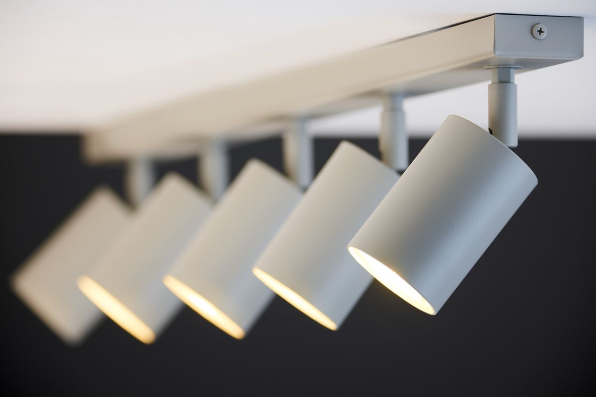 Lampa sufitowa Zoom w kolorze szaro-beżowym z pięcioma punktowymi źródłami światła GU10. Ujęcie z boku, pokazujące cylindryczne klosze oraz mocowanie do sufitu. Klosze są ustawione pod kątem, emitując światło w dół. Tło w ciemnym kolorze.