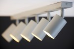 Lampa sufitowa Zoom w kolorze szaro-beżowym z pięcioma punktowymi źródłami światła GU10. Ujęcie z boku, pokazujące cylindryczne klosze oraz mocowanie do sufitu. Klosze są ustawione pod kątem, emitując światło w dół. Tło w ciemnym kolorze.