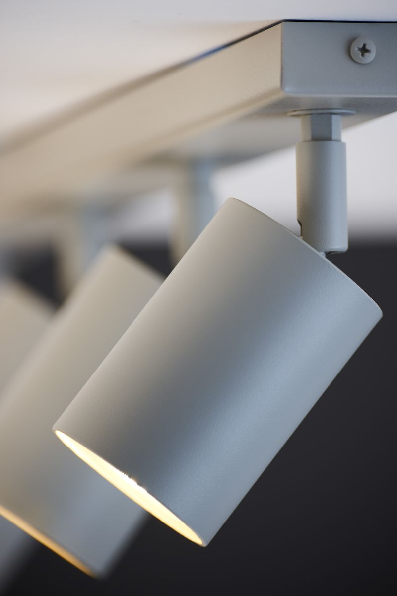 Lampa sufitowa Zoom w kolorze szarym beż, z pięcioma spotami GU10. Ujęcie z boku, zbliżenie na jeden z reflektorów, o cylindrycznym kształcie, zamocowany na metalowej podstawie. Jasne światło wydobywa się z oprawy.
