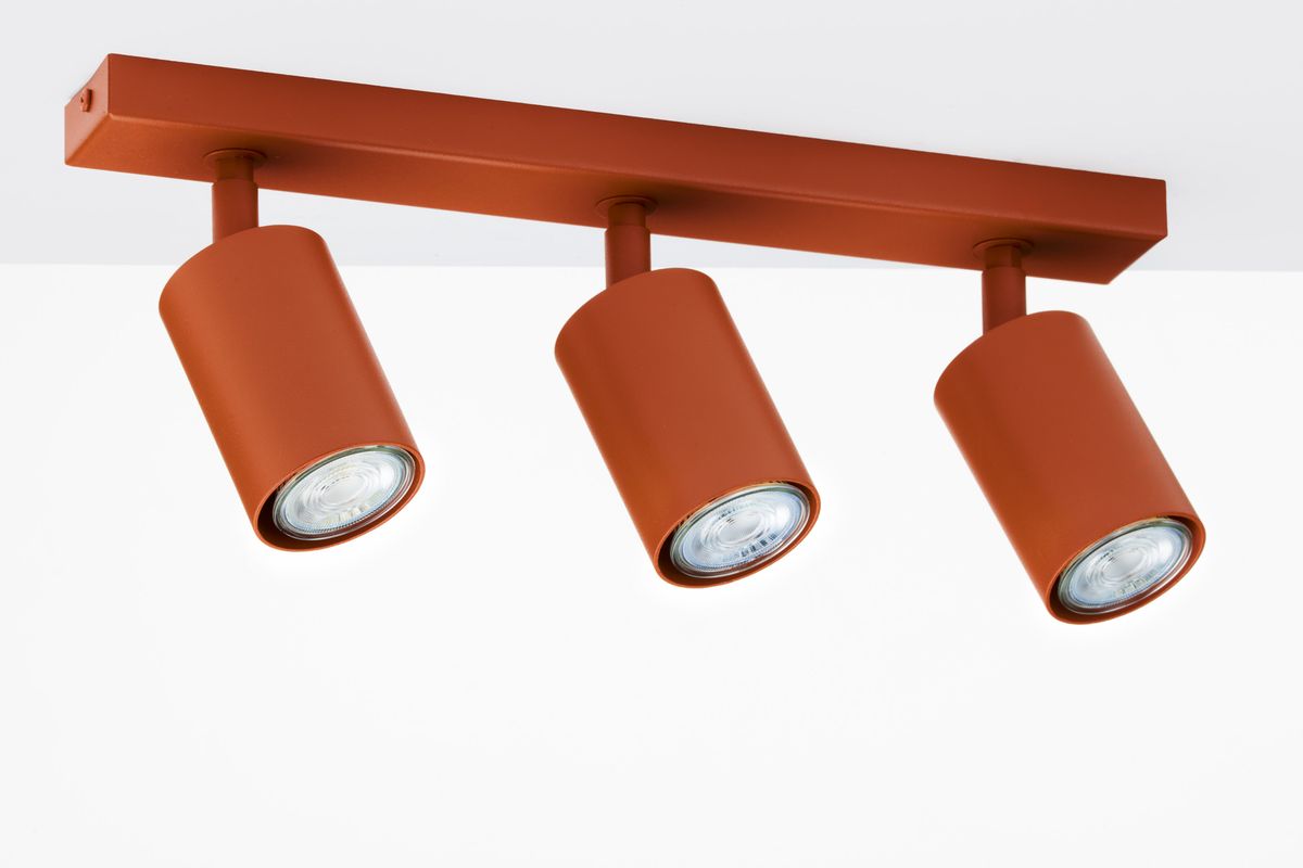 Lampa sufitowa Zoom z trzema reflektorami GU10 w ceglastym kolorze. Reflektory mają cylindryczny kształt i są zamocowane na prostokątnej podstawie. Ujęcie z dołu, ukazujące całość lampy na białym tle.