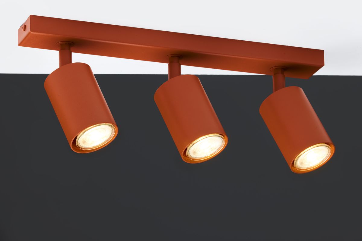 Lampa sufitowa Zoom w kolorze ceglastym z trzema reflektorami GU10. Reflektory mają cylindryczny kształt i są zamocowane na prostokątnej podstawie. Ujęcie z przodu na tle ciemnej ściany.