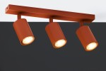 Lampa sufitowa Zoom w kolorze ceglastym z trzema reflektorami GU10. Reflektory mają cylindryczny kształt i są zamocowane na prostokątnej podstawie. Ujęcie z przodu na tle ciemnej ściany.