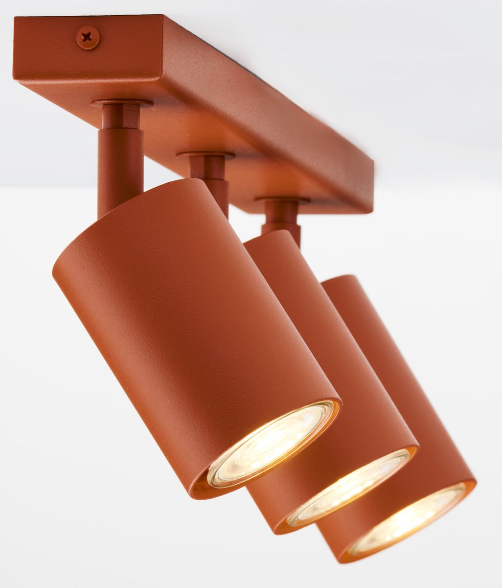 Lampa sufitowa Zoom z trzema reflektorami GU10 w ceglastym kolorze. Reflektory mają cylindryczny kształt, zamontowane na prostokątnej podstawie. Ujęcie z dołu, pod kątem, ukazujące szczegóły konstrukcji i źródła światła.