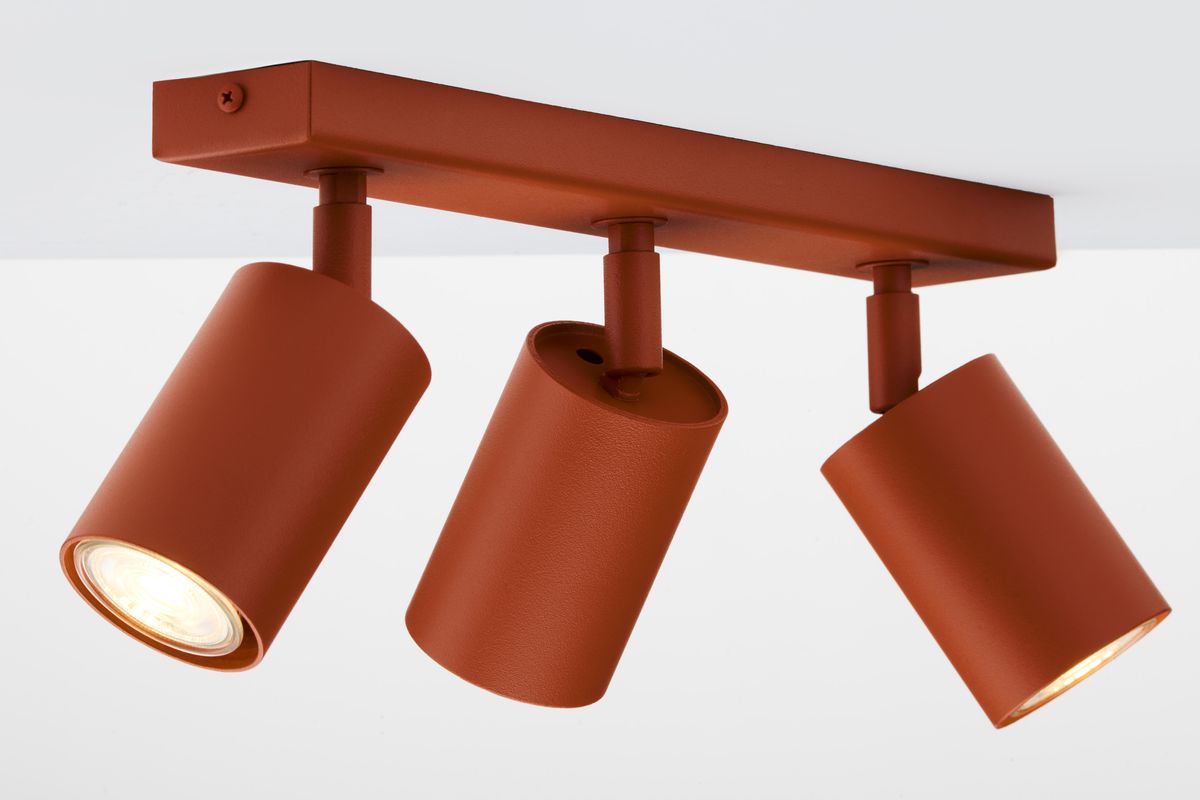 Lampa sufitowa Zoom w kolorze ceglastym z trzema ruchomymi reflektorami GU10. Ujęcie z boku, pokazujące okrągłe klosze z metaliczną fakturą, zamontowane na prostokątnej podstawie. Reflektory skierowane w różne strony, gotowe do oświetlenia przestrzeni.
