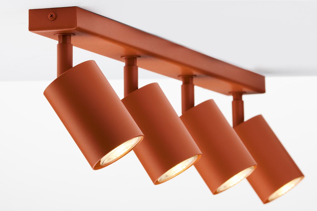 Lampa sufitowa Zoom w kolorze ceglastym z czterema reflektorami GU10. Ujęcie z przodu, pokazujące cylindryczne klosze umieszczone na metalowej listwie. Klosze są lekko nachylone, emitując ciepłe światło.