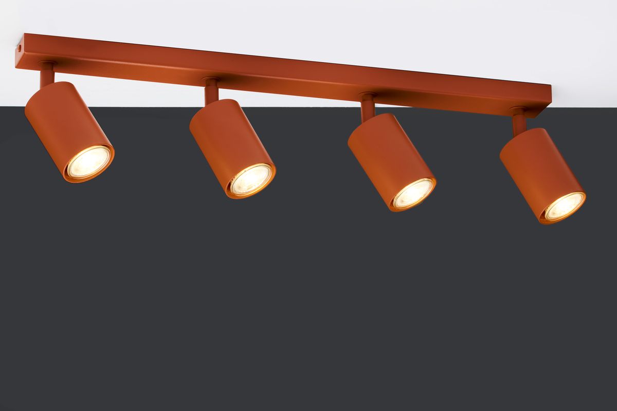 Lampa sufitowa Zoom w kolorze ceglastym z czterema reflektorami GU10. Ujęcie frontalne, lampy umieszczone na prostokątnej listwie. Widziane z góry, włączone, emitujące ciepłe światło na ciemnym tle.