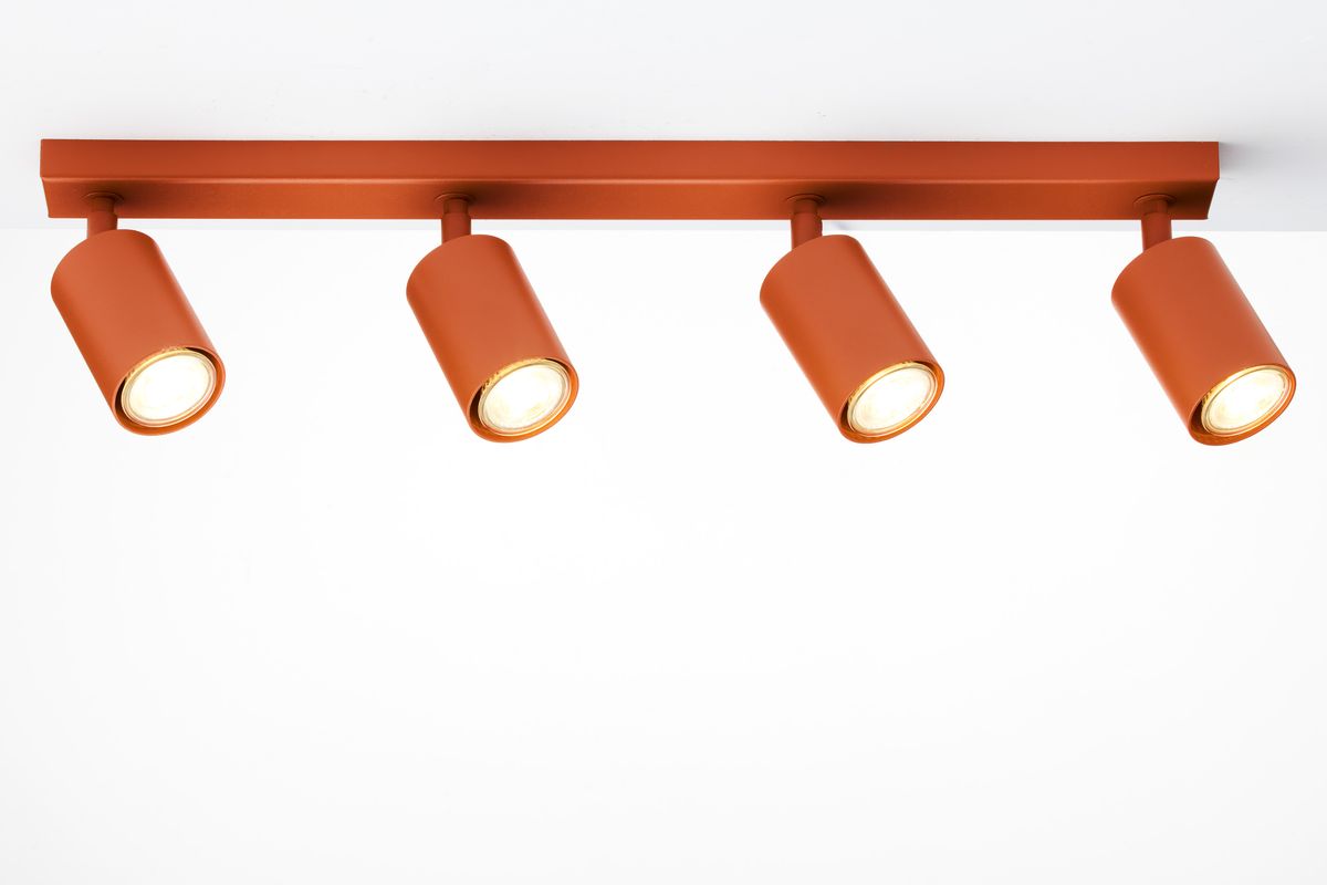 Lampa sufitowa Zoom w kolorze ceglastym z czterema punktami świetlnymi GU10. Ujęcie z góry, ukazujące prostokątną podstawę oraz cylindryczne klosze w pozycji wiszącej, emitujące jasne światło na białym tle.