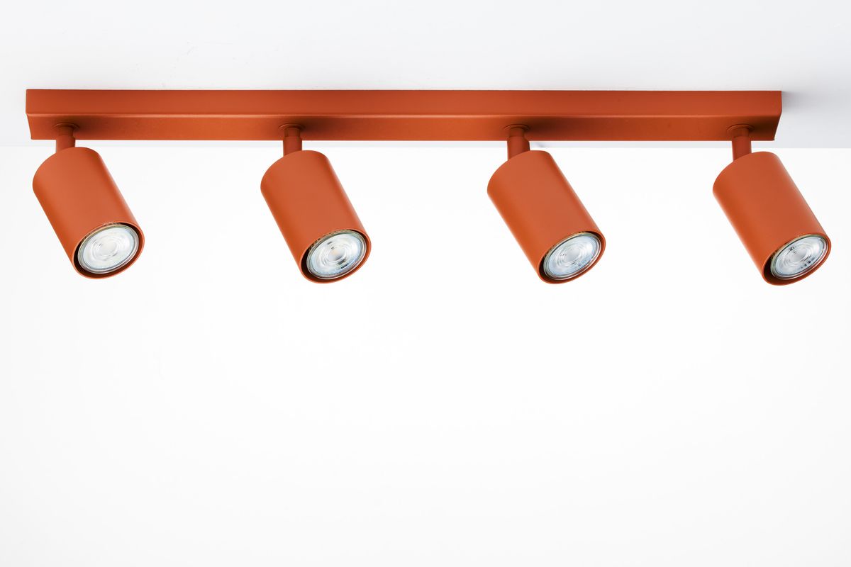 Lampa sufitowa Zoom z czterema reflektorami GU10, w kolorze ceglastym. Ujęcie frontalne, produkt zamontowany na suficie. Reflektory mają cylindryczny kształt i są skierowane w dół, na prostokątnej podstawie.