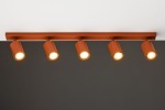 Lampa sufitowa Zoom w kolorze ceglastym z pięcioma reflektorami GU10. Ułożona poziomo na stelażu, każdy reflektor skierowany jest w inną stronę, co umożliwia regulację kierunku światła. Tło w ciemnym odcieniu podkreśla intensywność barwy lampy.
