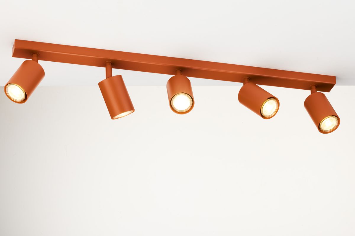 Lampa sufitowa Zoom w kolorze ceglastym z pięcioma spotami GU10. Ułożona poziomo, z widocznymi kloszami w formie walca, z matowym wykończeniem. Klosze skierowane w różne strony, zamocowane na prostokątnej listwie. Tło jasne, minimalistyczne.