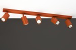 Lampa sufitowa Zoom w kolorze ceglastym, z pięcioma reflektorami GU10. Ułożona poziomo, z widocznymi cylindrycznymi kloszami. Tło w ciemnym kolorze, co podkreśla intensywność barwy lampy.