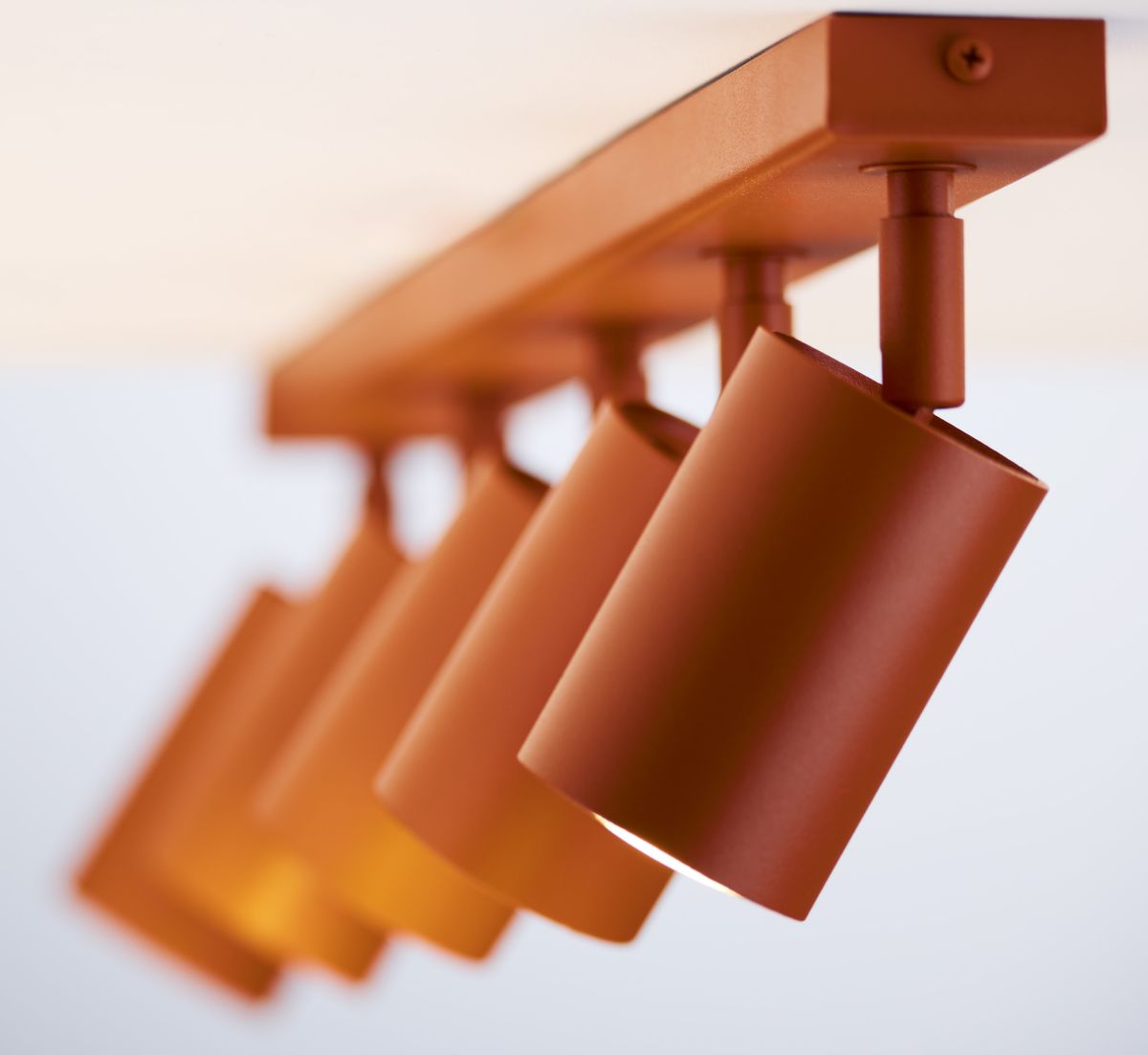 Lampa sufitowa Zoom z pięcioma spotami GU10 w ceglanym kolorze. Ujęcie z boku, pokazujące cylindryczne klosze zamocowane na prostokątnej listwie. Klosze mają matową powierzchnię, z widocznym źródłem światła.