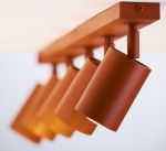 Lampa sufitowa Zoom z pięcioma spotami GU10 w ceglanym kolorze. Ujęcie z boku, pokazujące cylindryczne klosze zamocowane na prostokątnej listwie. Klosze mają matową powierzchnię, z widocznym źródłem światła.