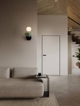 Kinkiet Casurno 1xLED 8W w kolorze czarnym i zielonym, z okrągłą, białą żarówką, zamontowany na ścianie. W tle widoczna szara sofa i drzwi w kolorze białym. Otoczenie nowoczesne, z drewnianymi detalami.
