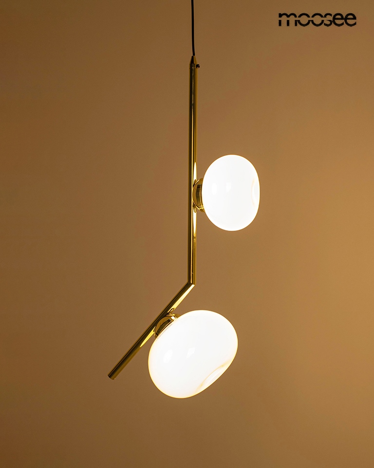 Lampa wisząca Rugia w kolorze złotym, z dwoma okrągłymi kloszami z białego szkła. Produkt zawieszony na cienkim przewodzie, w nowoczesnym stylu, idealny do aranżacji wnętrz. Klosze umieszczone na asymetrycznym ramieniu lampy.