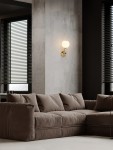 Laverzo kinkiet 1xLED 6W w kolorze złotym i beżowym, zamontowany na ścianie, z białym, okrągłym kloszem. W tle widoczna brązowa sofa i okna z żaluzjami. Kinkiet o minimalistycznym designie, zapewniający ciepłe światło.