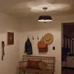Lampa wisząca Luella 3xE14 w kolorze czarnym i mosiężnym, umieszczona na suficie. Okrągły klosz zewnętrzny czarny, wewnętrzny biały. W tle widoczne ubrania na wieszakach oraz drewniana ławka z poduszkami.