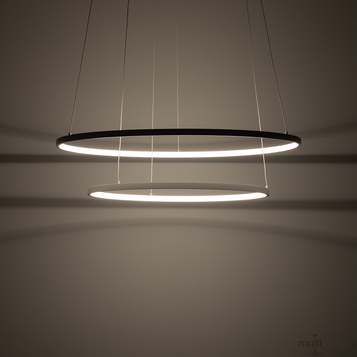 Lampa wisząca LED Circolo D60 o dwóch okrągłych pierścieniach w kolorze białym, zawieszona na cienkich linkach. Emituje ciepłe światło o temperaturze 3000K, tworząc subtelne cienie na ścianie. Idealna do nowoczesnych wnętrz.