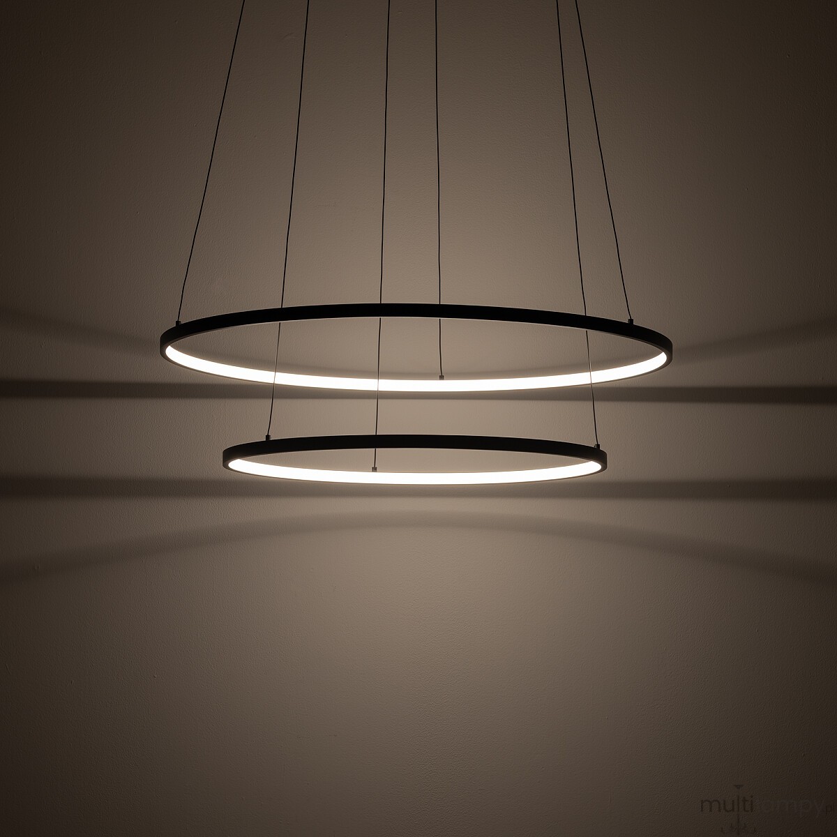 Lampa wisząca LED Circolo D60 o mocy 67W i barwie światła 3000K, w kolorze czarnym. Składa się z dwóch metalowych pierścieni, zawieszonych na cienkich linkach, rzucających delikatne cienie na ścianę.
