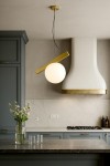 Lampa wisząca Balance 1xG9 w kolorze złotym, z okrągłą, białą szklaną kulą, zawieszona na cienkim przewodzie. Produkt umieszczony w nowoczesnej kuchni z szarymi frontami mebli i marmurowym blatem.