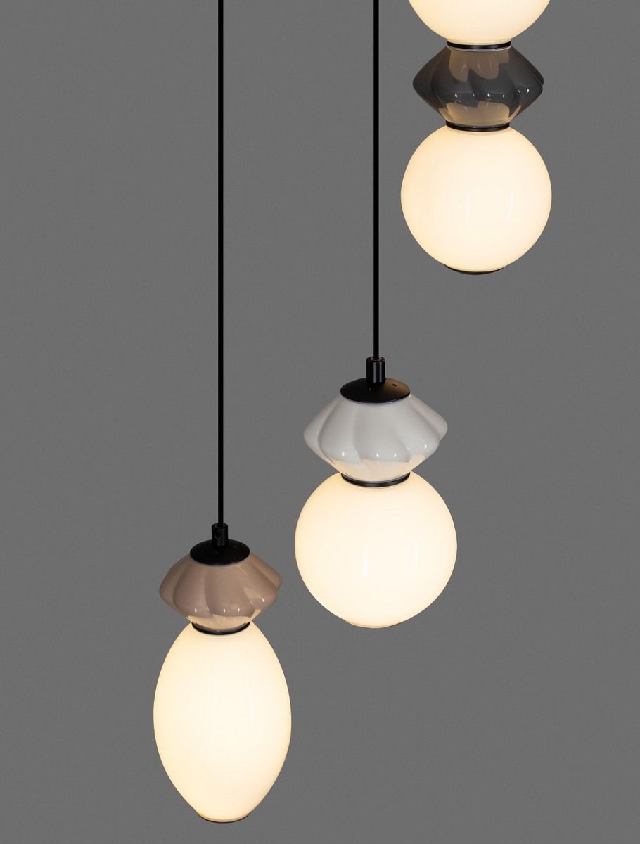Lampa wisząca Monreta z trzema kulistymi kloszami, zróżnicowanymi w kolorze białym, szarym i czarnym, zawieszona na czarnym przewodzie. Klosze mają różne kształty i są wykonane z materiału o połyskującej powierzchni.
