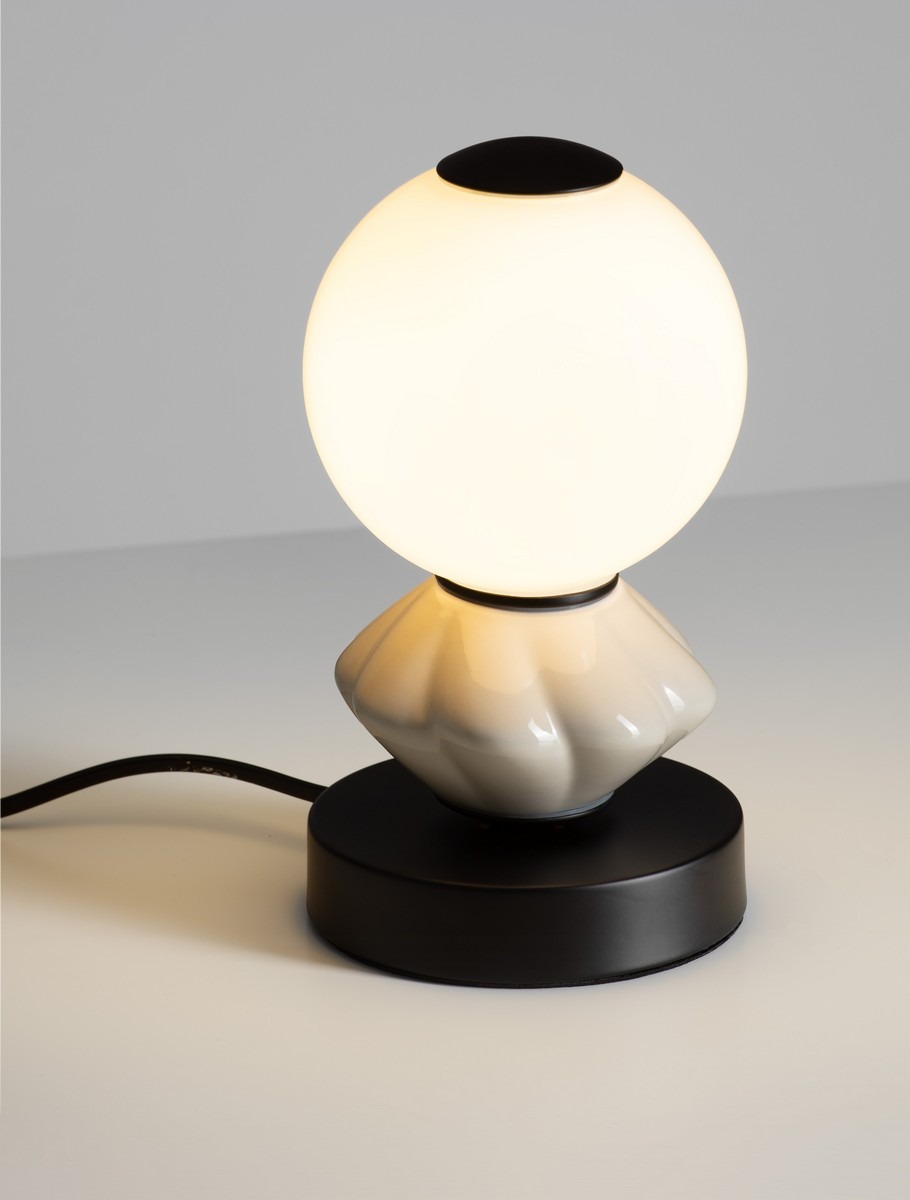 Lampa stołowa Monreta z czarną podstawą i jasnoszarym kloszem w kształcie kuli. Kluczowe elementy to szklany klosz emitujący ciepłe światło oraz elegancka, wypukła forma podstawy. Produkt ustawiony na jasnym tle.