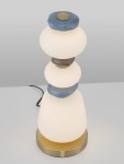Lampa stołowa Felanzo z jedną żarówką LED 23W. Okrągła, biała szklana podstawa z dekoracyjnymi, kolorowymi elementami (niebieskim i brązowym). Metalowa, złota podstawa. Ujęcie z góry, na białym tle.