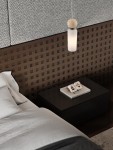 Lampa wisząca Corvizo 1xG9 w kolorze złotym, z matowym szklanym kloszem i dekoracyjną kulą u góry. Zawieszona nad czarną szafką nocną, w aranżacji sypialni z teksturowanym tłem w odcieniach brązu.