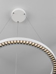 Lampa wisząca Tarvana z białym okrągłym kloszem, zawieszona na cienkich linkach. Wyposażona w 27W LED, na obrzeżu klosza dekoracyjne, złote elementy. Widoczny sufit z jasnym tłem.