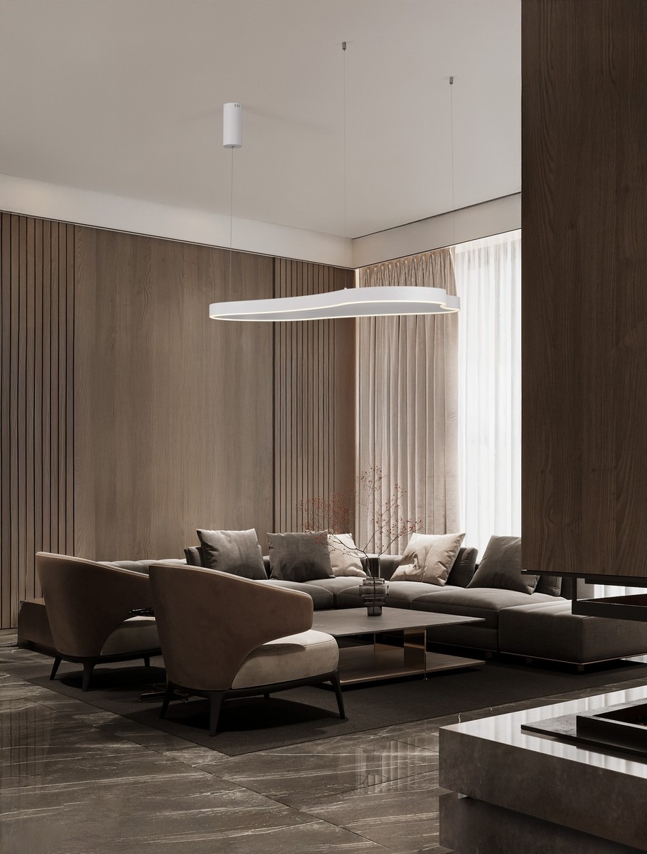 Lampa wisząca Velbano 1xLED 61W w kolorze białym, o nowoczesnym, smukłym kształcie, zawieszona na cienkim przewodzie. Widoczna w eleganckim wnętrzu z ciemnymi elementami drewnianymi i sofą z poduszkami, na tle jasnych zasłon.