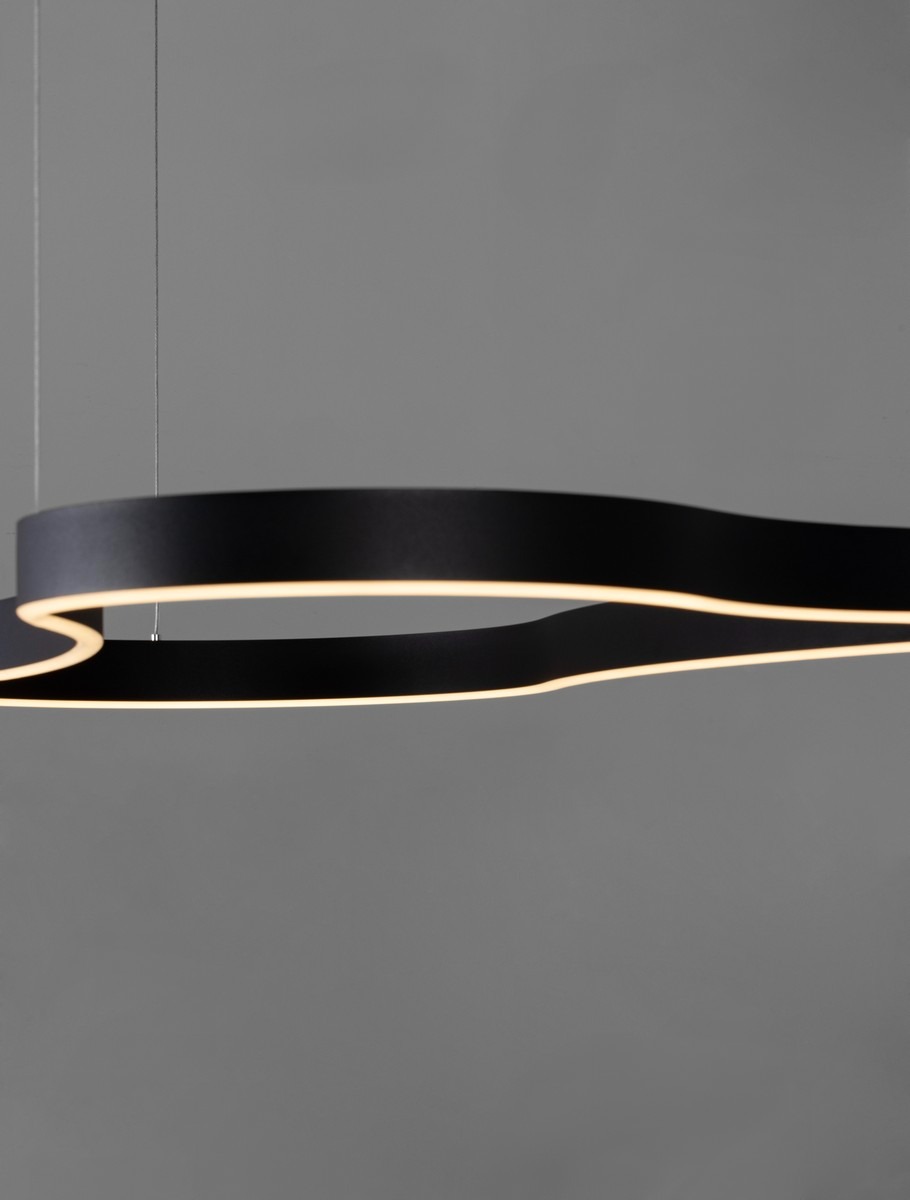 Lampa wisząca Velbano 1xLED 61W w kolorze czarnym, o nowoczesnym, falistym kształcie. Zawieszona na cienkich linkach, emitująca ciepłe światło z wbudowanego źródła LED. Tło w odcieniu szarości, podkreślające minimalistyczny design.