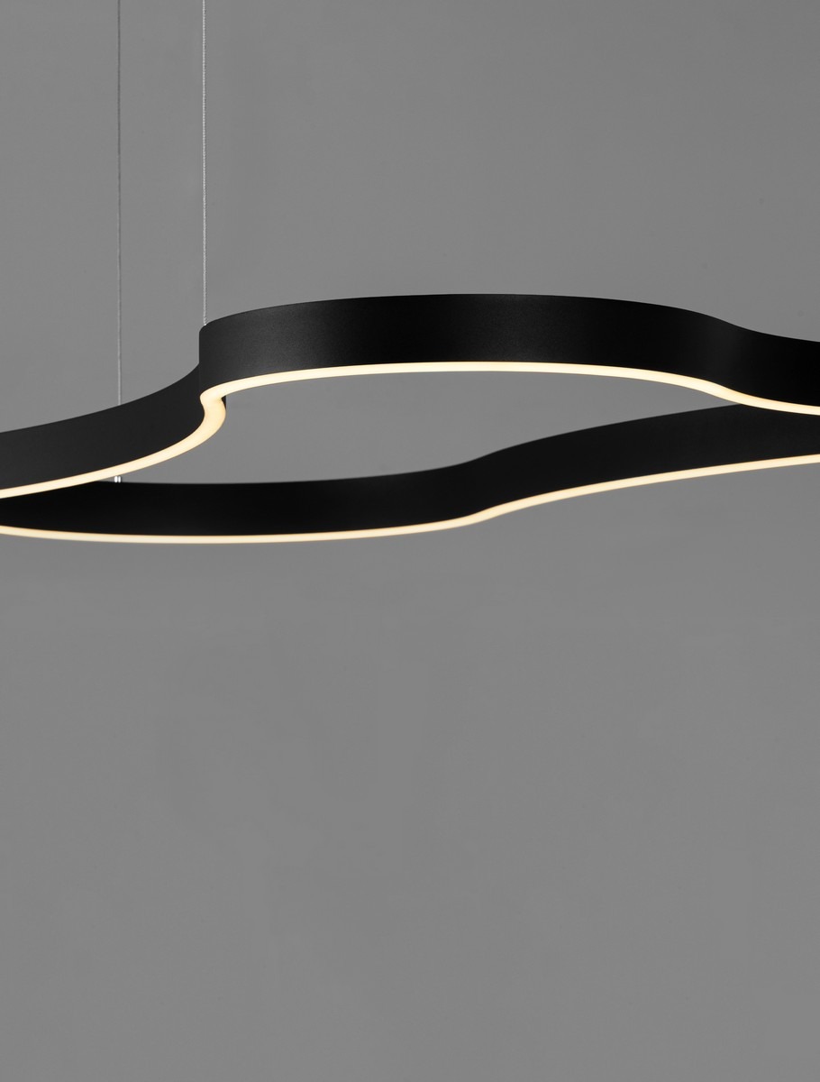 Lampa wisząca Velbano w kolorze czarnym, z LED 61W. Ma nowoczesny, falisty kształt z subtelnym podświetleniem. Zawieszona na cienkich linkach, idealna do nowoczesnych wnętrz. Tło w odcieniach szarości.