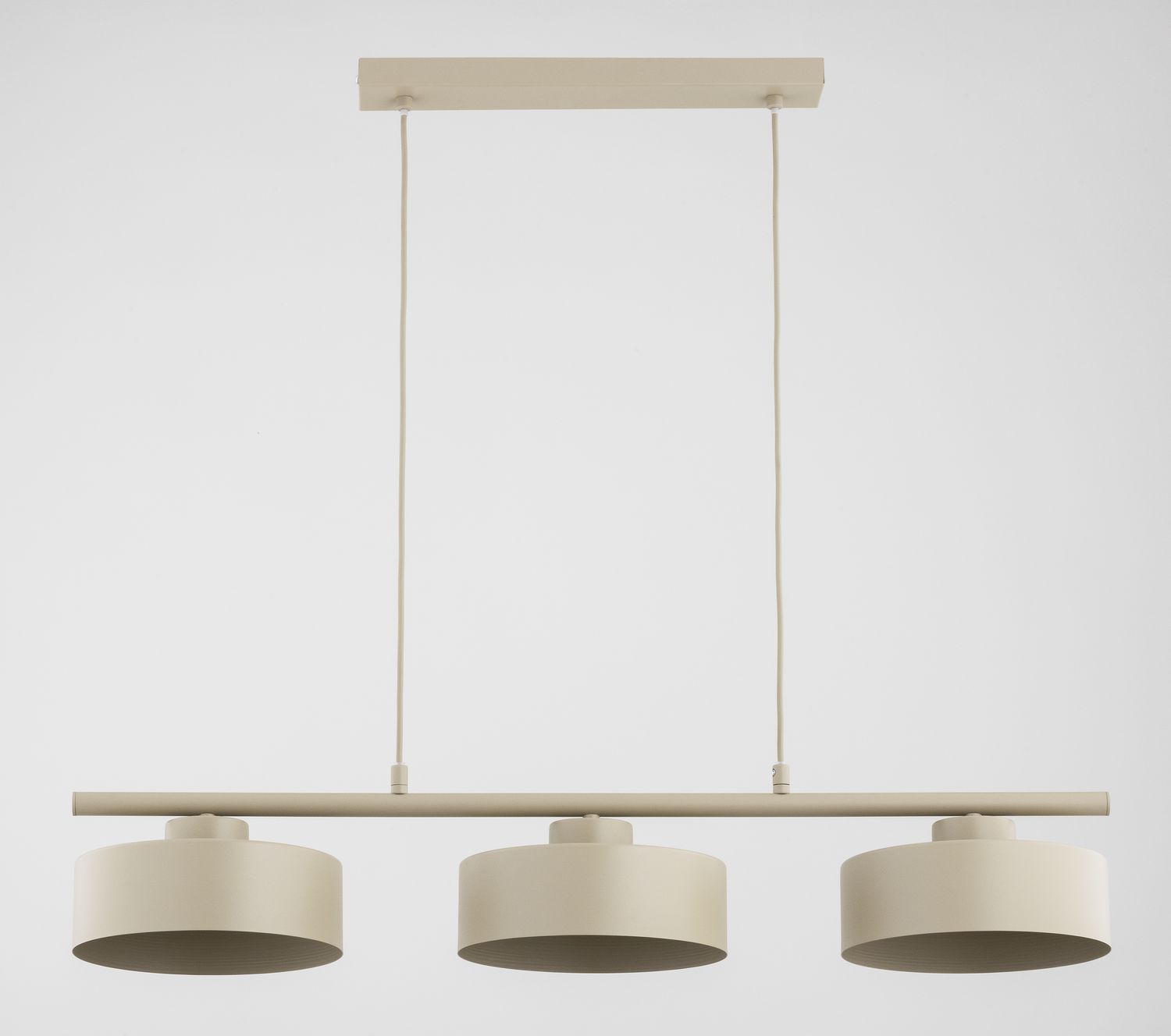 Beżowa lampa wisząca Selia z trzema oprawami E27, zawieszona na cienkich linkach, z prostą metalową belką. Klosze w kształcie cylindrów, matowe, z delikatną teksturą. Produkt wisi na jednolitym tle, podkreślając minimalistyczny design.