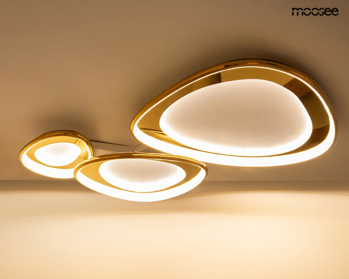 Lampa sufitowa Cell 3 w kolorze złotym z trzema elementami o organicznych kształtach. Wyposażona w technologię LED 120W i pilot do zdalnego sterowania. Ujęcie z dołu, na jednolitym tle, z widocznym podświetleniem.