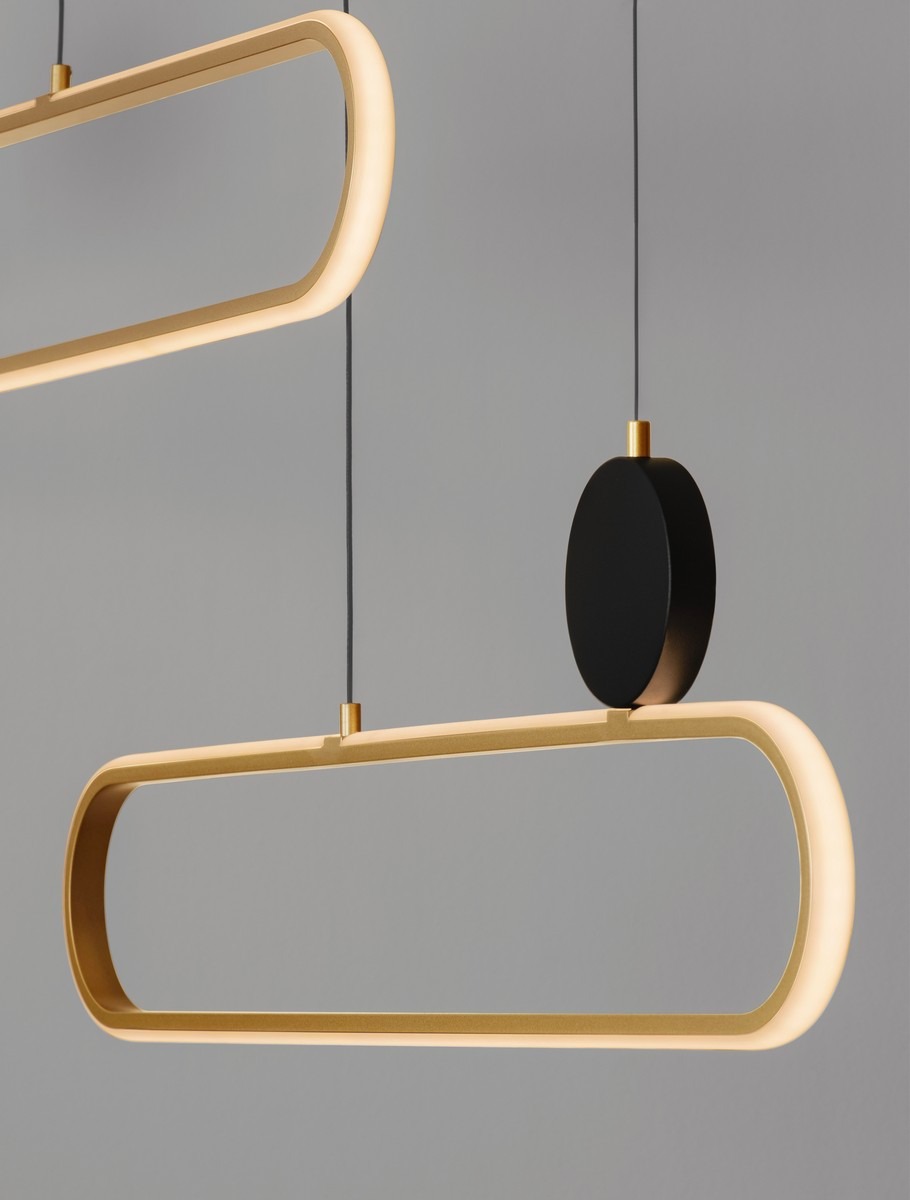 Lampa wisząca Turviano z dwoma źródłami LED 49W, w kolorze czarnym i złotym. Posiada nowoczesny, prostokątny kształt z podświetleniem oraz okrągłe mocowanie. Zawieszona na cienkim przewodzie, na szarym tle.