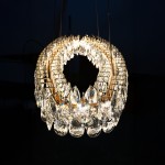 Lampa wisząca Barletta D120 w kolorze złotym, z jedną diodą LED o mocy 120W. Okrągła konstrukcja zdobiona kryształowymi elementami w kształcie kropli, zawieszona na cienkich linkach, emitująca jasne światło. Tło ciemne.