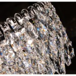 Lampa wisząca Burano D60 w chromowanym wykończeniu, z 11 miejscami na żarówki E14. Zbliżenie na dekoracyjne, przezroczyste kryształy w kształcie rombów, odbijające światło i tworzące efektowną grę kolorów.