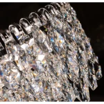 Lampa sufitowa Burano D100 o chromowanej podstawie, z 28 uchwytami E14. Zbliżenie na kryształowe elementy w kształcie rombów, odbijające światło, tworzące efekt tęczy. Produkt wiszący, idealny do eleganckich wnętrz.