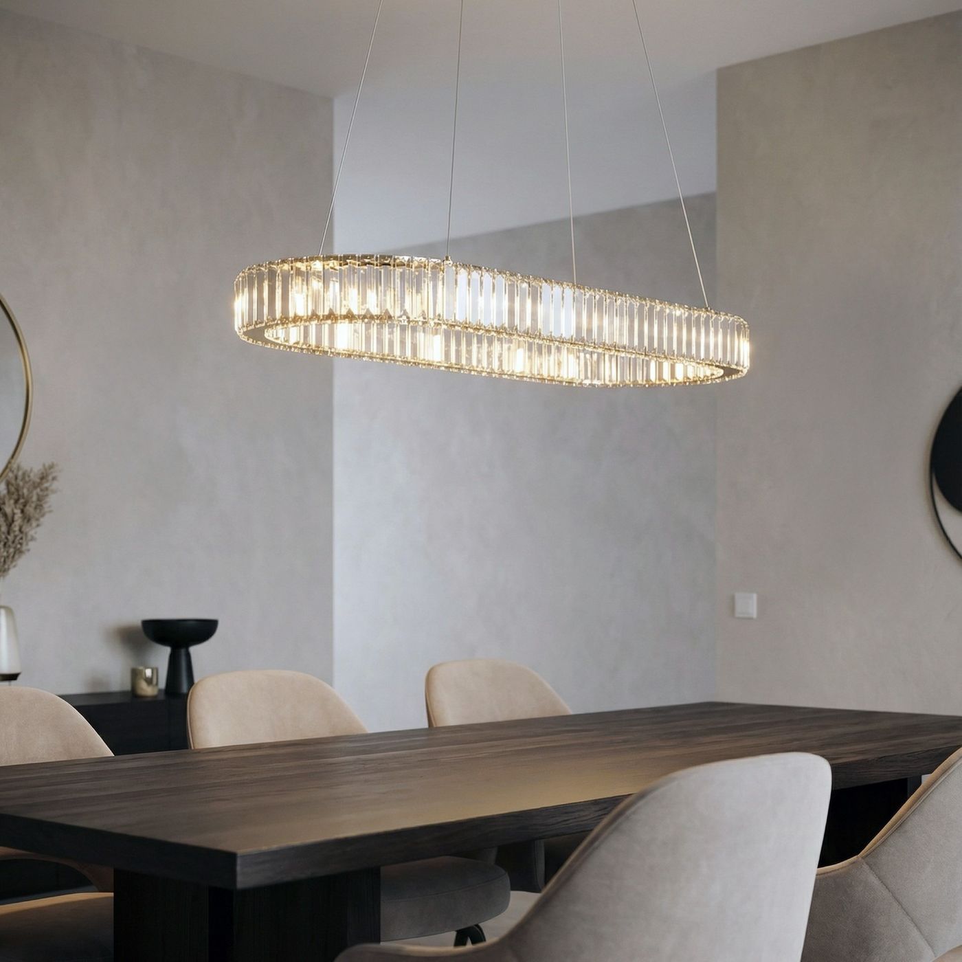 Lampa wisząca Spark Oval w złotym kolorze, o opływowym kształcie, zawieszona nad drewnianym stołem. Zawiera dwa źródła LED 78W CCT. Tło w jasnych odcieniach, na ścianie widoczny okrągły lustro i dekoracyjne elementy.