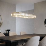 Lampa wisząca Spark Oval w złotym kolorze, o opływowym kształcie, zawieszona nad drewnianym stołem. Zawiera dwa źródła LED 78W CCT. Tło w jasnych odcieniach, na ścianie widoczny okrągły lustro i dekoracyjne elementy.