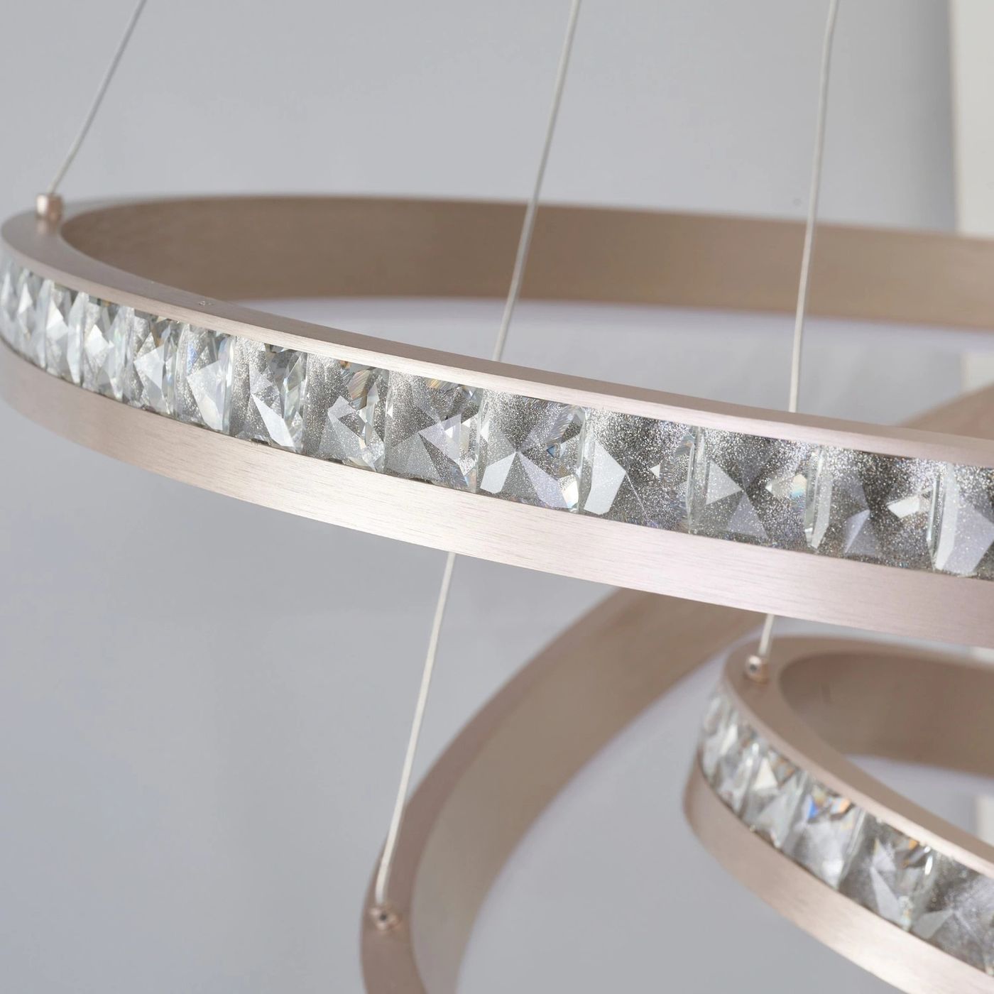 Lampa wisząca Camelia z jedną diodą LED o mocy 41W, złota konstrukcja z metalowym obręczami, ozdobiona kryształowymi detalami, zawieszona na cienkich linkach, w zbliżeniu na teksturę i wykończenie.